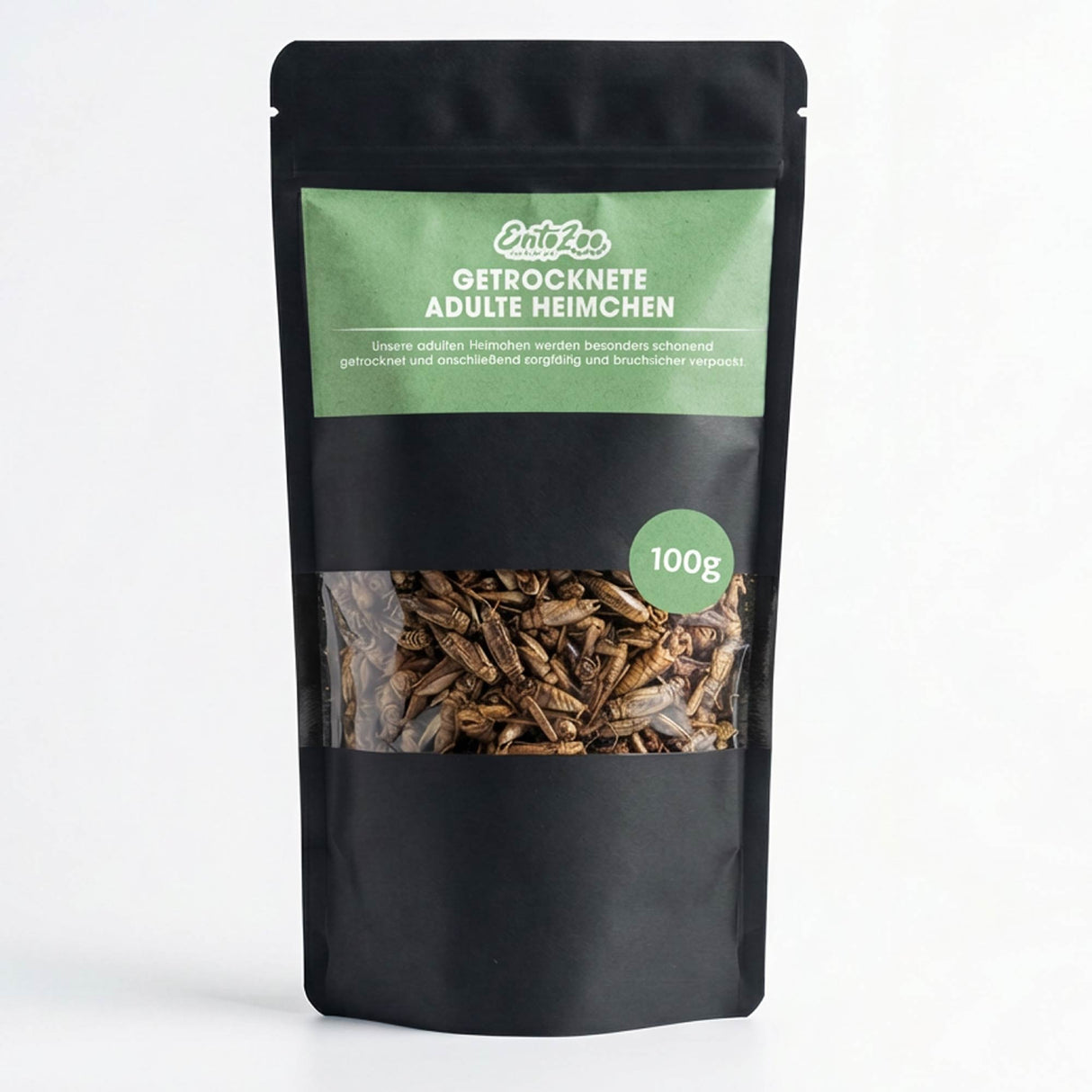 Produktbild einer 100 g Packung getrockneter Heimchen (Acheta domesticus). Die Heimchen befinden sich in einem schwarzen Standbodenbeutel mit grünem EntoZoo Etikett und Sichtfenster, durch das die Insekten sichtbar sind. Auf der Verpackung steht „Getrocknete adulte Heimchen“. Die Packung eignet sich als Tierfutter für verschiedene Tierarten wie Reptilien, Geflügel oder Wildvögel. Zentrale Aussage: kompakte und praktische Packung hochwertiger getrockneter Heimchen als Insektenfutter.